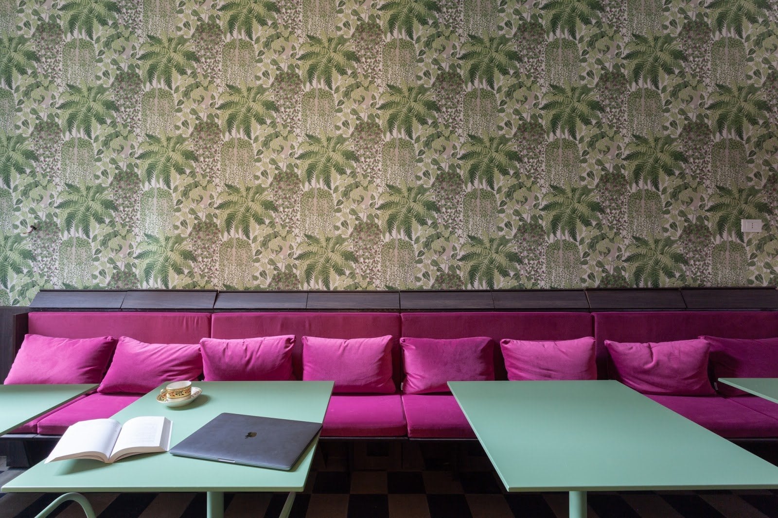 BeetCommunity coliving lounge with magenta velvet banquette, mint-green tables and palm-leaf wallpaper in Palermo