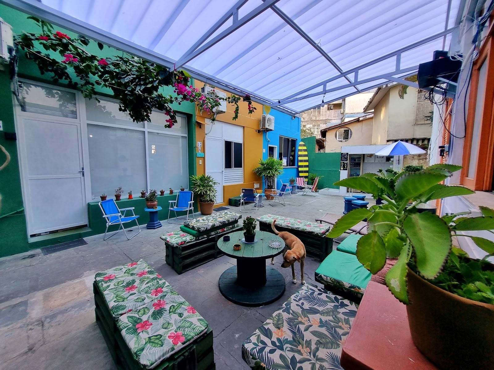 Colourful covered courtyard lounge with tropical-print seating and plants at Nomads Multiespaço, Salvador