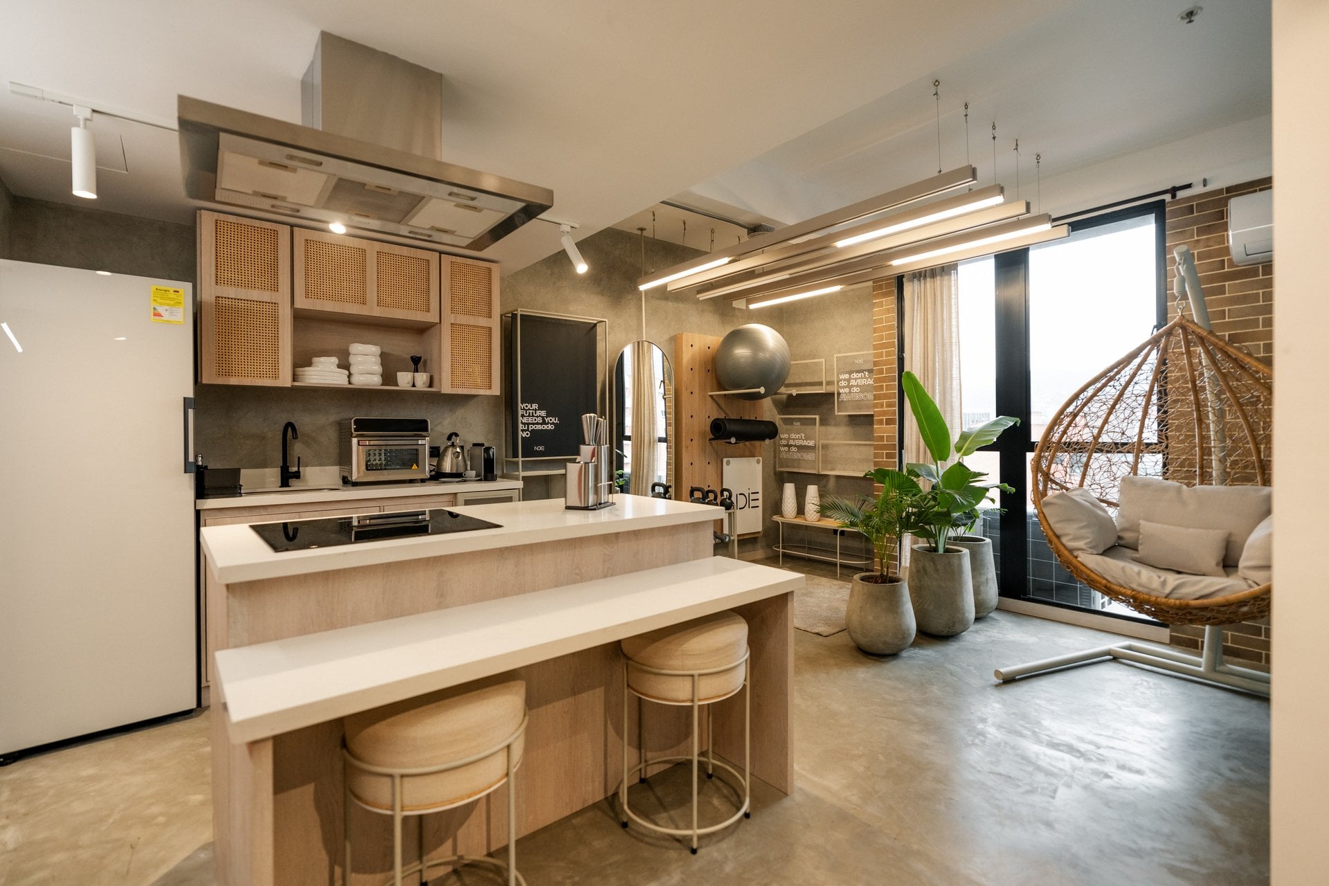 Sunlit Wellness suite at Indie Studio with a rattan hanging chair, plants and open kitchen by floor-to-ceiling windows in Medellín
