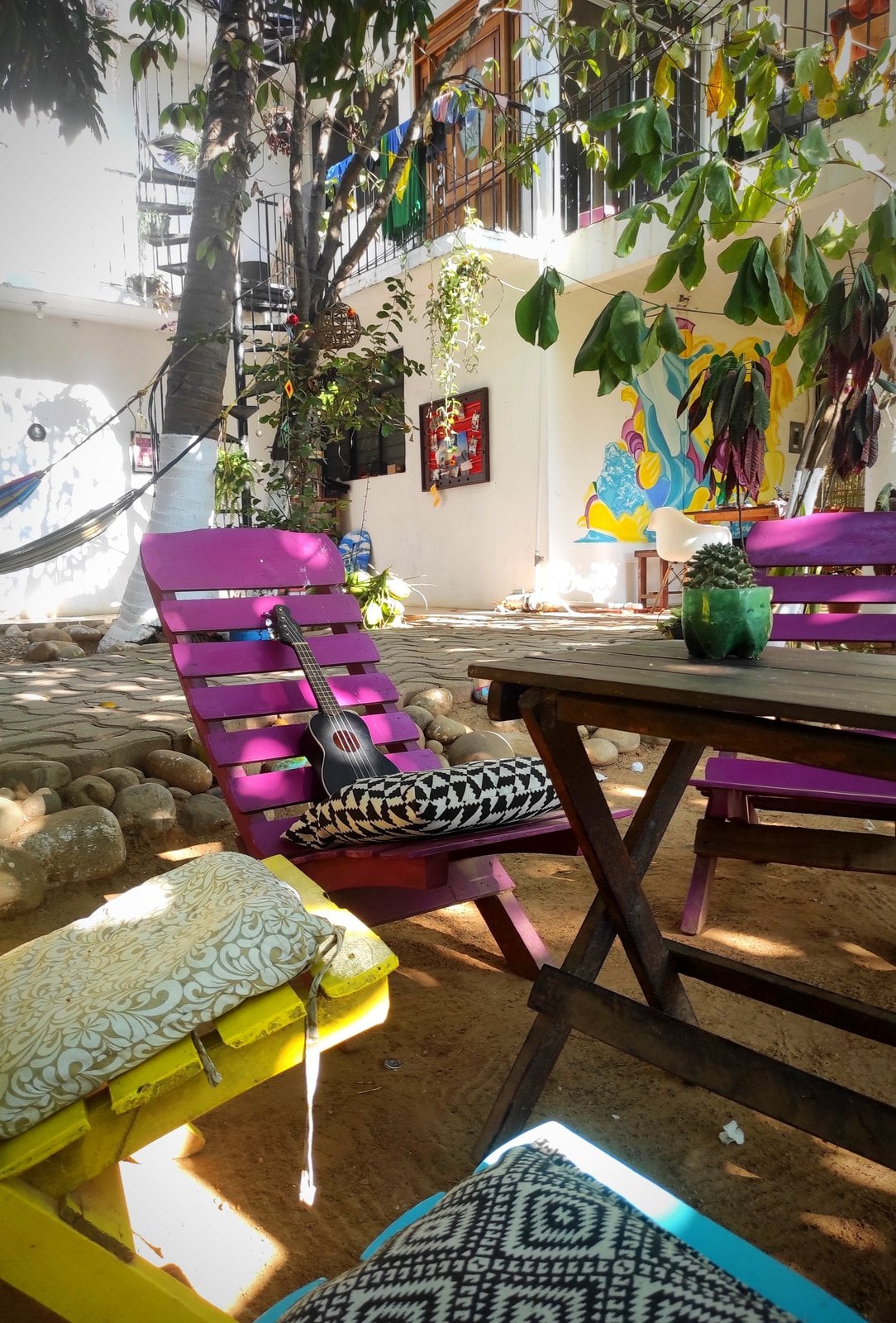Colorful courtyard at El Mundito Coliving — hammocks, purple sun loungers, guitar, and tropical murals in Puerto Escondido
