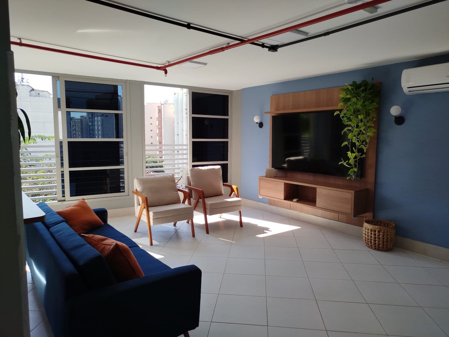 Sunlit communal TV lounge with blue sofa and armchairs at Vivére Coliving in Rio de Janeiro