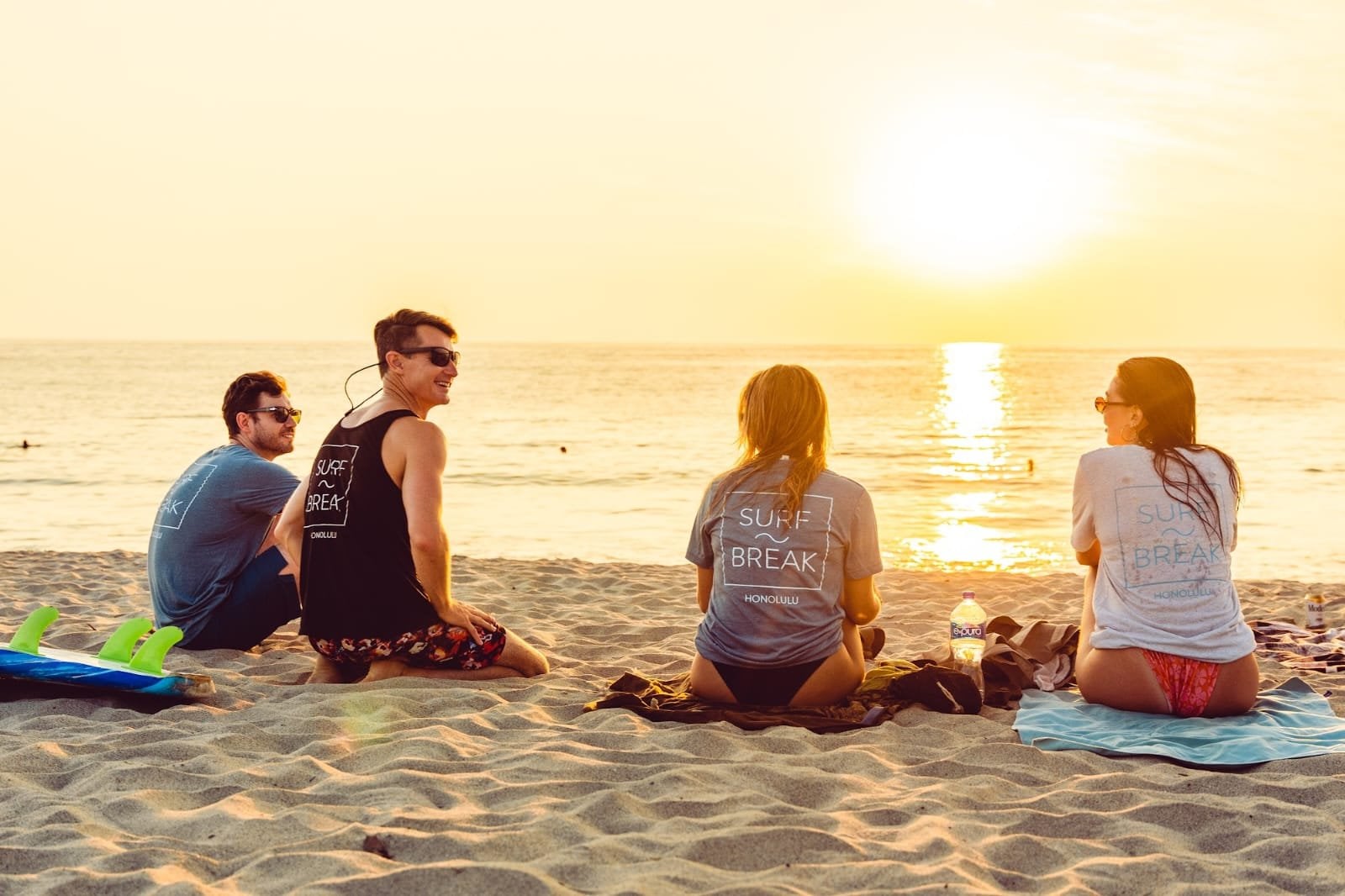 Four Surfbreak PXM residents relaxing on the beach at sunset wearing Surfbreak shirts