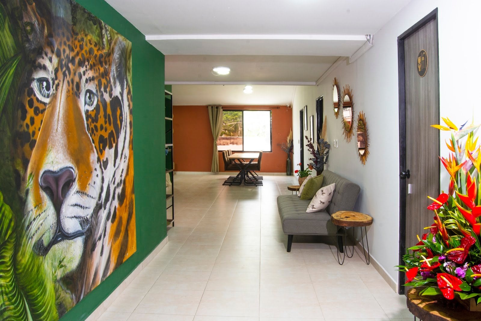 Bright lobby lounge at Bohemia Boutique Hostel Cali with large jaguar mural, sofa and tropical flowers