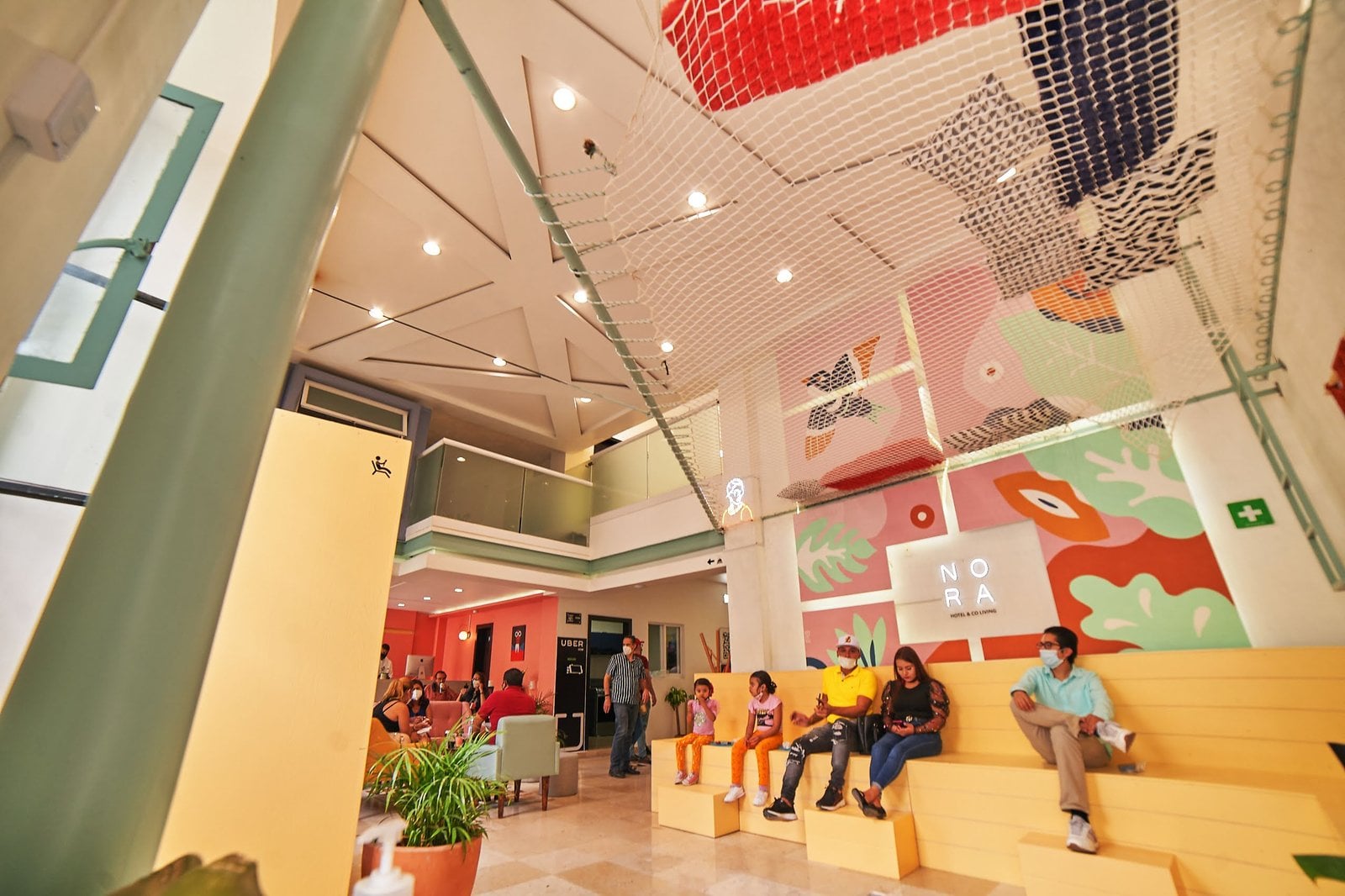 Residents relaxing and socializing in the vibrant common area at Nora Hotel Coliving Guadalajara, under the iconic ceiling net with colorful murals