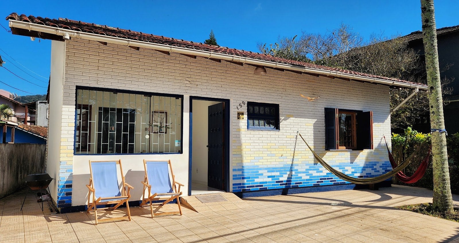 Sunlit deck with lounge chairs and a hammock against the blue wave-tiled facade at Casa Maré coliving in Florianópolis
